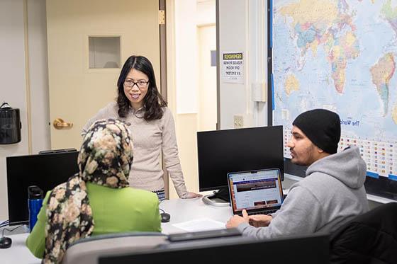 An instructor and students speak together in a computer lab